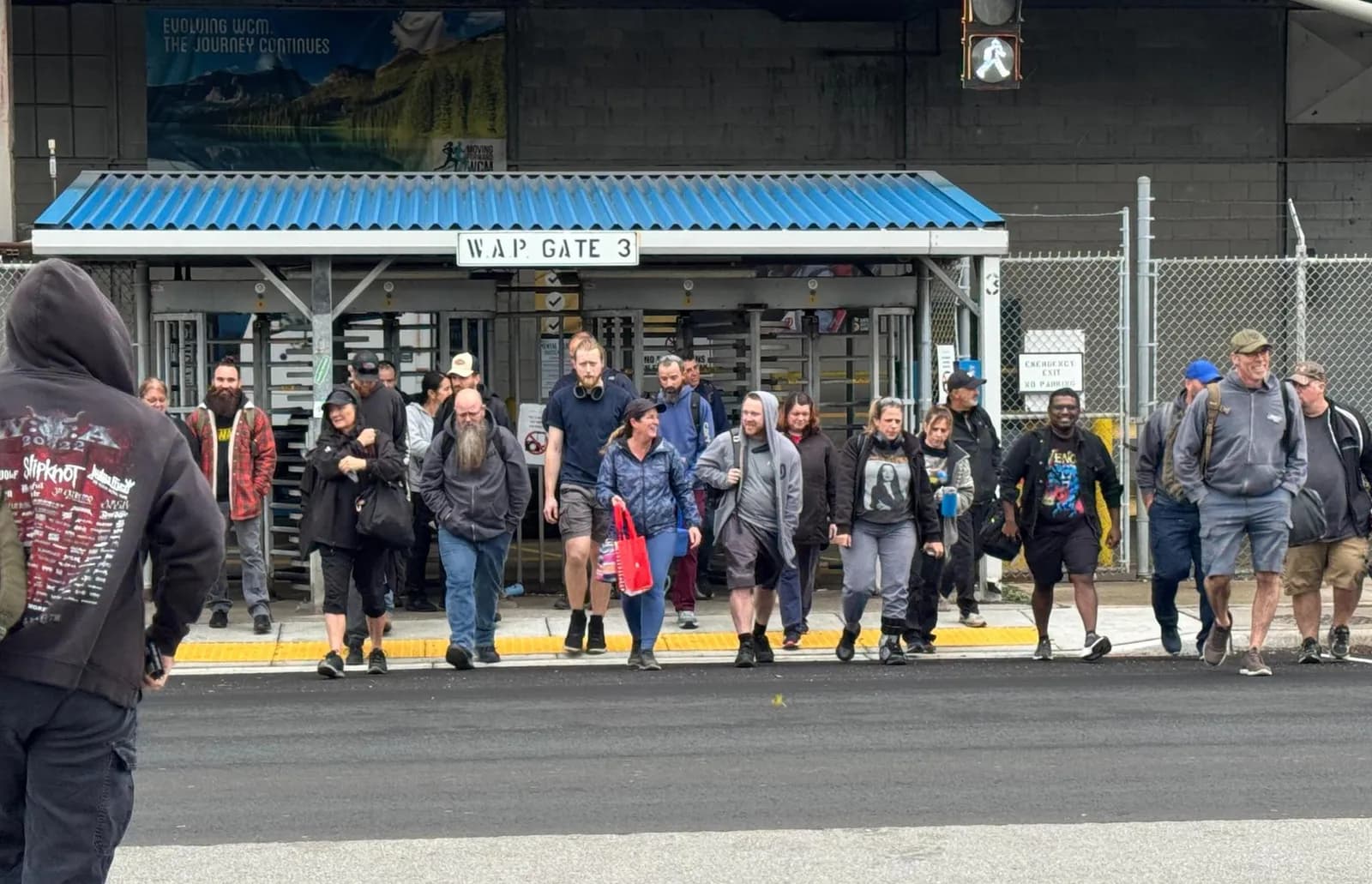 Workers stream out of Gate 3 of the Stellantis Windsor Assembly Plant at shift change, under a blue corrugated awning and a sign reading “W.A.P. Gate 3.”