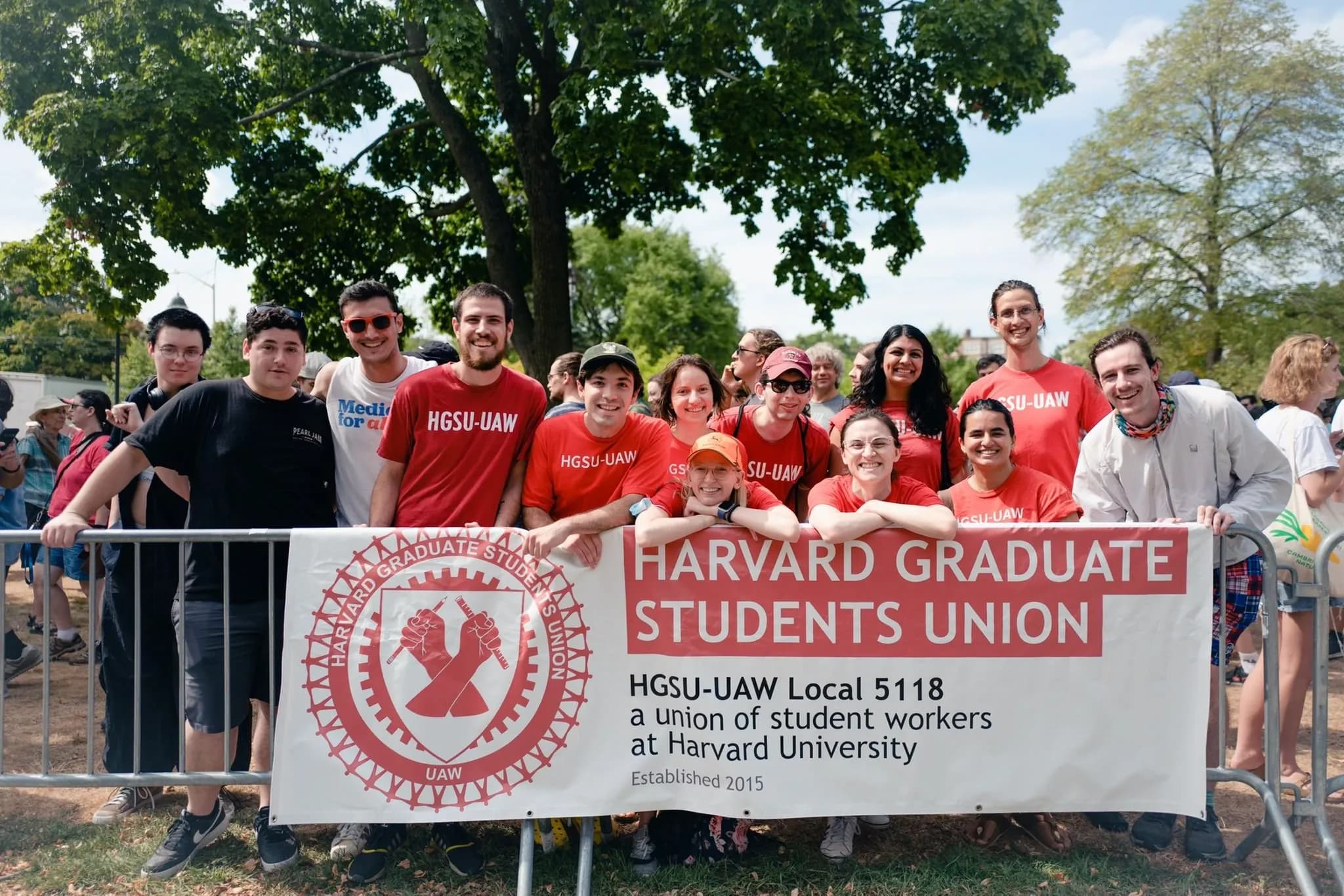A group of Harvard graduate student workers in red HGSU-UAW t-shirts posing behind a banner reading 'Harvard Graduate Students Union — HGSU-UAW Local 5118, a union of student workers at Harvard University, Established 2015'