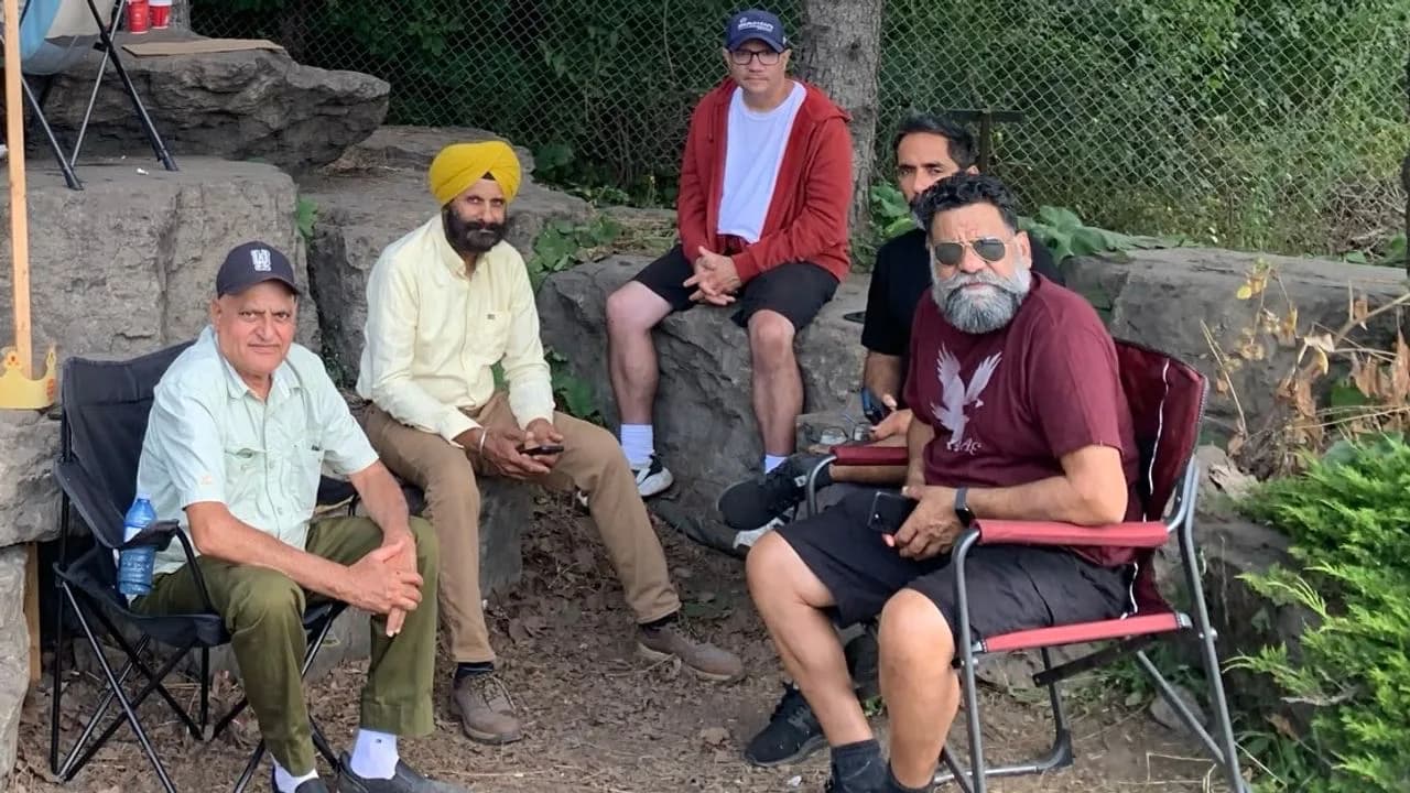 Five National Steel Car strikers sit together on camp chairs and a stone ledge beside a chain-link fence at the picket line in Hamilton, Ontario.