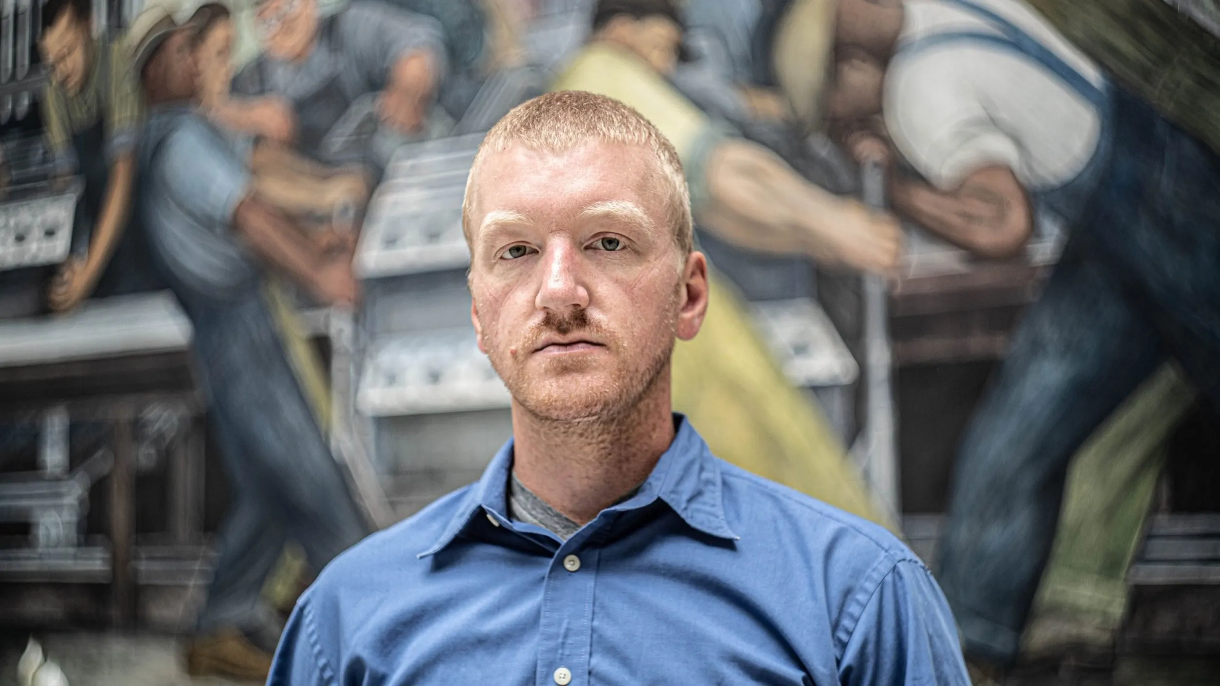 Will Lehman standing in front of the Detroit Industry Murals at the DIA
